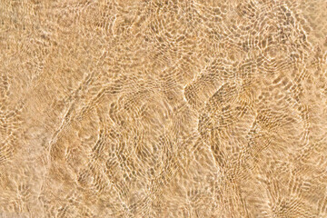 Crystal clear sea water surface with sunlit ripples tropical nature background. Rippled effect on yellow sand beach, backdrop with sunlight reflection underwater, transparent aqua texture pattern.
