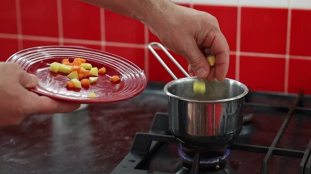 Close up male hands of a cook adding diced vegetables to a vegan soup. Bachelor man lunch.