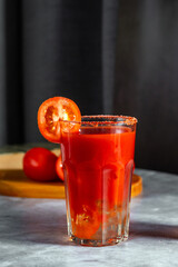 Vegetable shaken cocktail in glass on dark grey background. Red tomato cocktail. Served with tomato slice. Vegan menu.