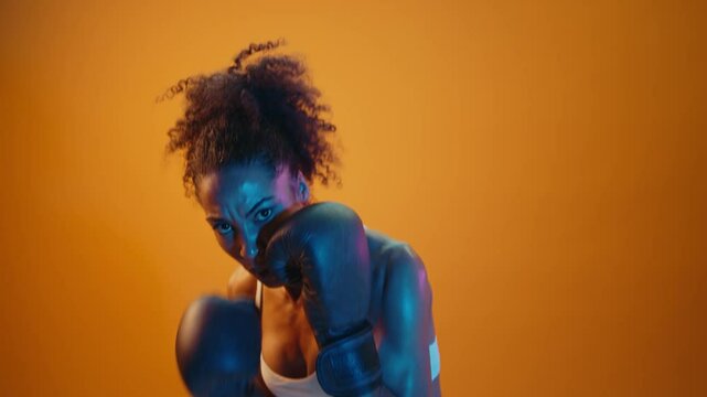 Sportive black hispanic woman wearing sportswear training boxing in fitness studio, colorful dramatic lighting - African-american female athlete doing sport workout	