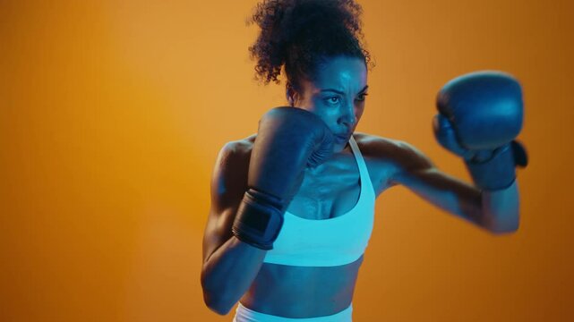 Sportive black hispanic woman wearing sportswear training boxing in fitness studio, colorful dramatic lighting - African-american female athlete doing sport workout	