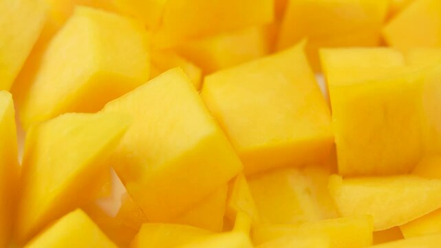 A close up of yellow mango slices. The slices are cut into cubes and are spread out on a white surface