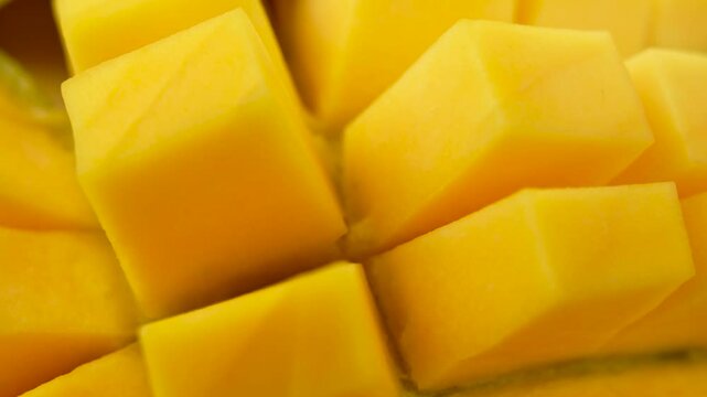 A slice of yellow mango with a green stem. The mango is cut into small cubes