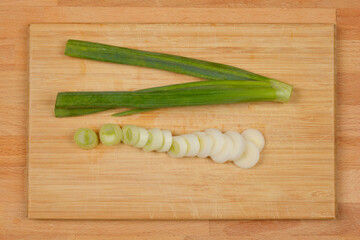 A top-down shot of a spring onion, both whole and sliced, on a wooden cutting board, showcasing its fresh green color and preparation.