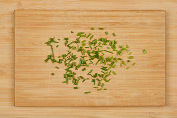 Finely chopped chives are arranged in the center of a square wooden cutting board, viewed from above