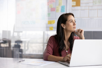 Thoughtful ambitious Hispanic business leader woman working at computer, looking away, touching chin, thinking on project management, planning successful strategy. Candid shot with copy space