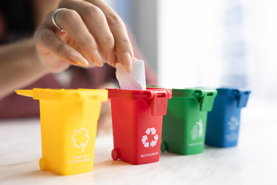 Woman promoting waste sorting, recycling, putting garbage into one of four colorful tiny toy trash bins, caring for environment future, sustainable development. Close up of hand