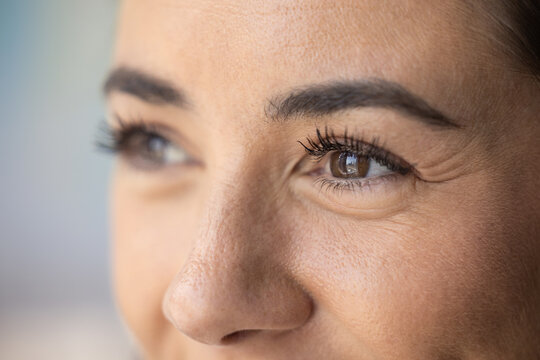 Brown eyes of young mid adult woman with smile wrinkles and black mascara on curled eyelashes. Upper female face cropped macro shot. Model looking away, promoting eye care, eyesight, beauty care
