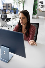 Serious online teacher giving business webinar on Internet. Busy Hispanic sales manager talking to company client on video chat, using wireless headset with mic and desktop monitor