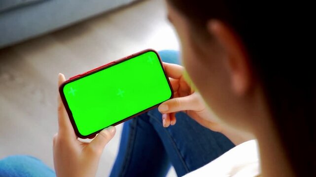 4K footage of a woman holding a smartphone with green screen while sitting indoors, perfect for app mockups, video overlays, UI demos, mobile marketing, and chroma key projects