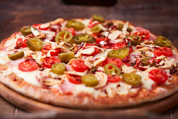 Pizza with ham, cherry tomatoes and mozzarella cheese. Wooden background. Soft focus. Close up.