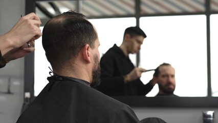 Skilled barber trimming client's hair using professional scissors, creating precise hairstyle in contemporary salon with modern interior and relaxed atmosphere