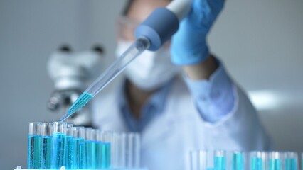 Close up of a female scientist researcher hand using a micropipette to fill up test tubes with a blue liquid in laboratory. Medicine and science