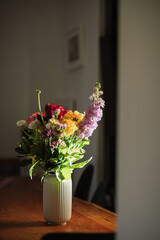 A bouquet of beautiful flowers in a vase, placed on a table at home. The soft morning light gently illuminates the flowers, creating a warm and serene atmosphere in the room.
