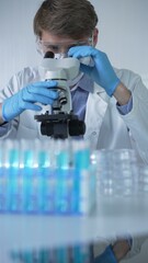 Male scientist researcher wearing lab coat, blue protective gloves, medical mask and glasses, is...