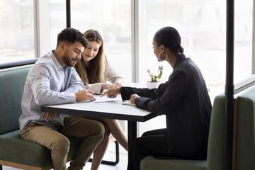 Young couple finish negotiations with professional real estate agent or financial advisor signing...
