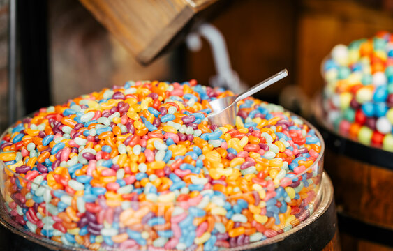 A bowl filled with colorful jelly beans sits at a candy shop. A metal scoop rests on top, inviting customers to enjoy a variety of sweet, chewy, and vibrant treats.