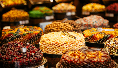 An assortment of dried fruits and confections beautifully arranged in wooden barrels at a market. The colorful display includes apricots, berries, nuts, and candied treats.