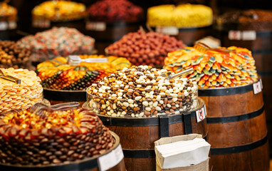 A vibrant selection of gourmet dried fruits, nuts, and chocolate-coated treats arranged in wooden barrels at a market. The colorful display creates an inviting and festive atmosphere.