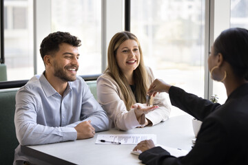 Smiling millennial couple finalize deal with real estate agent professional or sales manager,...