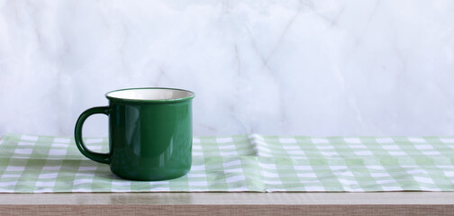 Green enamel mug sitting on checkered cloth and wooden table