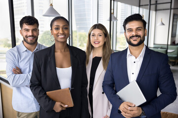 Cheerful diverse group of confident, multinational business professionals standing together in modern coworking office, posing for corporate photo. Successful teamwork, leadership, and collaboration