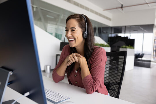 Cheerful online teacher woman in wireless headphones speaking at monitor, giving online training, talking to audience on video conference chat, smiling. Happy support manager laughing at workplace