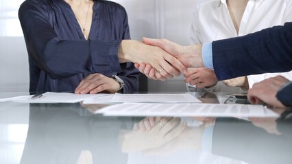 Unrecognizable business partners shaking hands after signing contract at glass table in office meeting, making a deal and closing agreement, close up of handshake