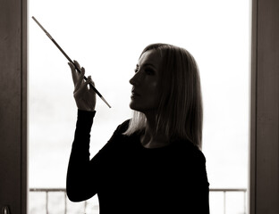 Obraz premium A portrait of a beautiful woman against the light, holding a cigarette holder