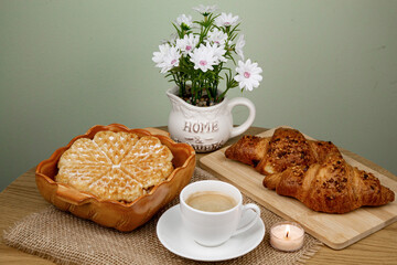 A cup of coffee, waffles and croissants on the table. Breakfast with coffee