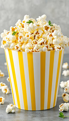 Buttery popcorn overflowing a yellow striped container, garnished with herbs, against a gray background