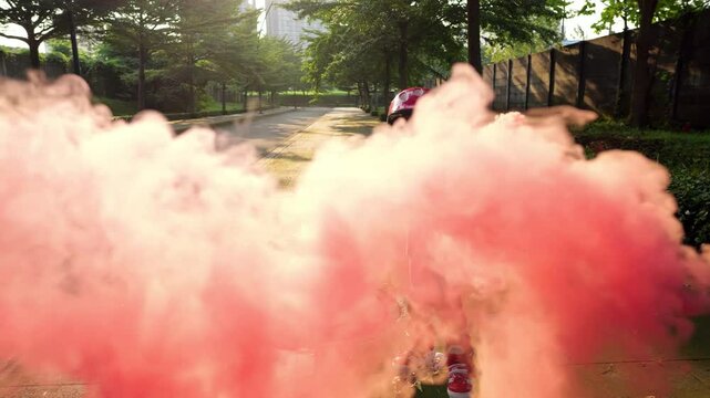Sunlight filtering through billowing red smoke, young rollerblader creating vibrant clouds and trail, holding stick with attached smoke bomb. Little cheerful boy embodying childhood energy