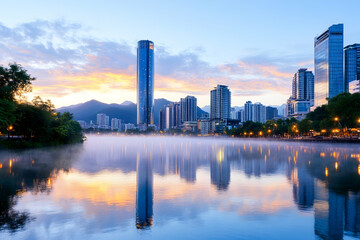 Fototapeta premium Misty sunrise over a city skyline reflected in calm water