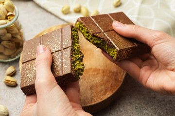 Woman breaking Dubai chocolate bar with pistachio and knafeh at grey table, closeup