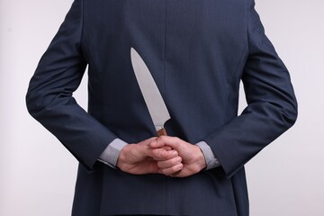 Businessman holding knife behind his back on white background, closeup