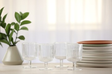 Empty clean glasses, plates and green branches on table indoors