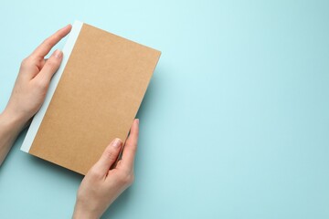 Obraz premium Woman with copybook on light blue background, top view. Space for text