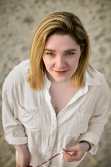 Young woman with blonde hair stands pensively on serene beach. Her relaxed expression reflects...