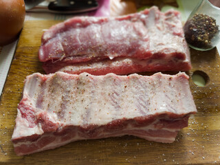 Raw pork ribs pieces sprinkled with spices on cutting board