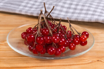 Ripe viburnum berries on saucer on rustic table, close-up