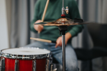 Obraz premium A person in casual attire passionately plays the drums, highlighting the cymbal in a cozy studio setting. The image captures the essence of musical practice and artistic dedication.