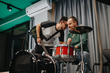 Two musicians share a fun and energetic moment practicing together with a guitar and drum set. The...