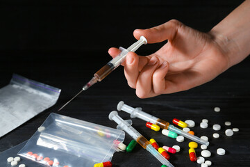 Drug addiction. Woman with syringe at black wooden table against dark background, closeup