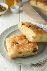 Pieces of delicious focaccia bread with olives, thyme and salt on white wooden table, closeup