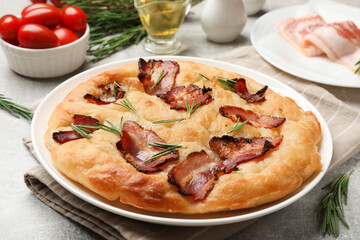 Delicious focaccia bread with bacon, rosemary, oil and tomatoes on light grey table, closeup