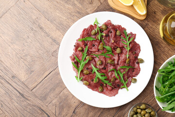 Fresh beef carpaccio with arugula and capers on wooden table, flat lay. Space for text