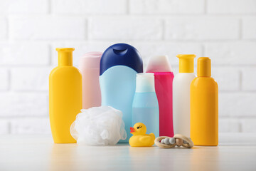 Baby cosmetic products, shower puff, rattle and rubber duck on table against white brick wall