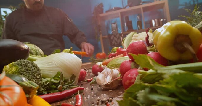 Time-lapse shot of a skilled chef slicing a carrot on wooden chopping board. Chef preparing salad as the camera moving forward through the vegetable row