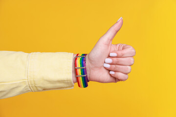 Woman wearing wristband in LGBT colors and showing thumbs up on orange background, closeup