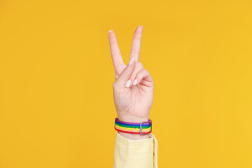 Woman wearing wristband in LGBT colors and showing peace sign on orange background, closeup